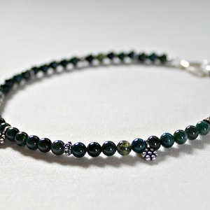 May include: A green agate beaded bracelet with silver accents. The bracelet has a clasp closure and is adorned with small silver charms.