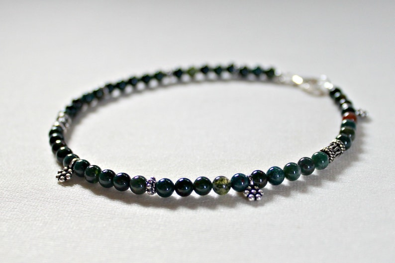 May include: A green agate beaded bracelet with silver accents. The bracelet has a clasp closure and is adorned with small silver charms.