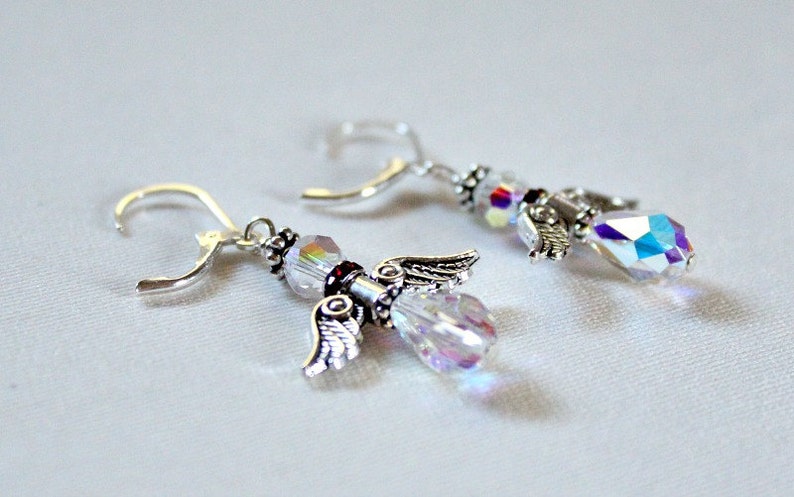 May include: A pair of silver angel wing earrings with clear iridescent crystal beads and a small red bead accent.