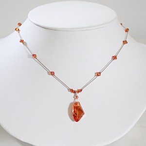 May include: A delicate necklace with a copper-toned chain and small, faceted orange beads. A large, faceted orange crystal hangs from the center of the chain.