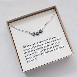 May include: A small box with a silver necklace featuring three hematite heart charms. The box includes a card with the text: "Hematite is a protective stone that promotes healing and inner peace. It is the most grounding stones among all. Hematite is a calming stone which brings balance between the body, mind and spirit."