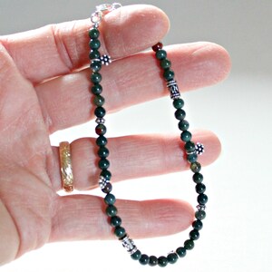 May include: A green and silver beaded bracelet with silver flower and geometric charms. The bracelet is made with small round beads and is approximately 8 inches in length.