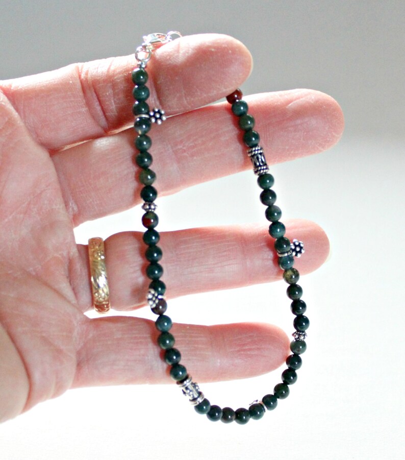 May include: A green and silver beaded bracelet with silver flower and geometric charms. The bracelet is made with small round beads and is approximately 8 inches in length.