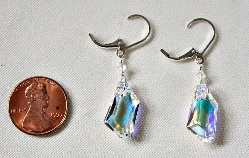 May include: A pair of silver dangle earrings with iridescent crystal teardrop pendants. The earrings are approximately the size of a US penny.