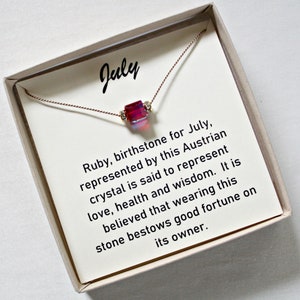 May include: A small red gemstone necklace in a white box with the text "July" and a description of the gemstone, "Ruby, birthstone for July, represented by this Austrian crystal is said to represent love, health and wisdom. It is believed that wearing this stone bestows good fortune on its owner."