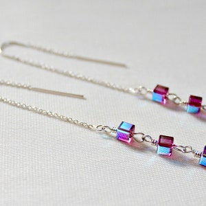 May include: A pair of silver dangle earrings with a chain and four iridescent purple and blue square-shaped beads.