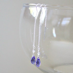 Puede incluir: Un par de pendientes de plata con un cristal morado en forma de lágrima al final de cada cadena.