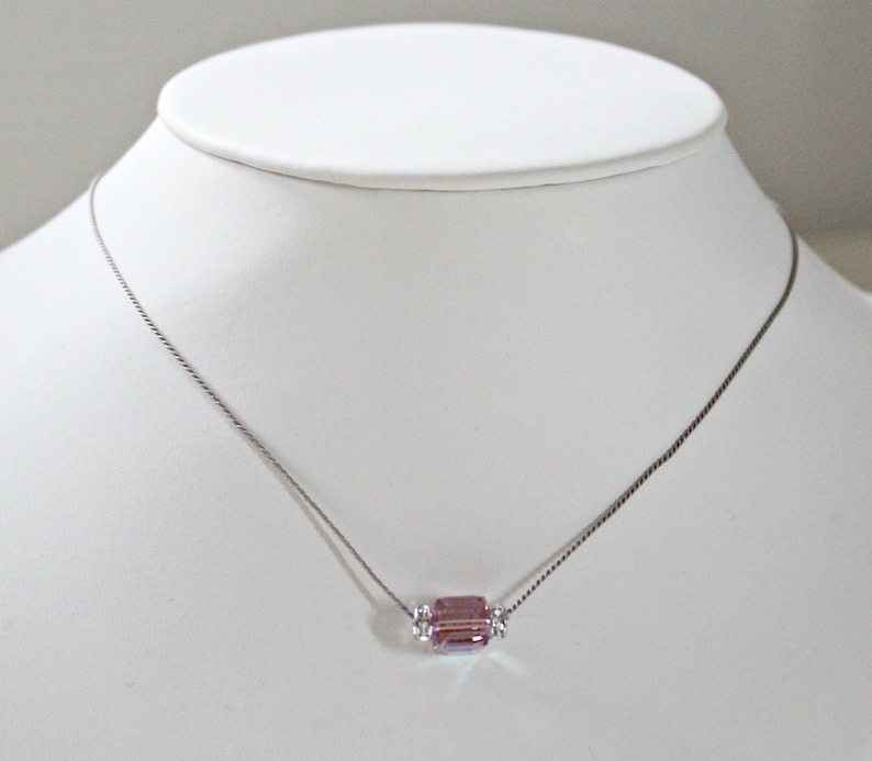 May include: A delicate silver chain necklace with a single, faceted, light purple crystal pendant.