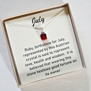 May include: A silver necklace with a small, rectangular, ruby-colored pendant. The pendant is displayed in a gift box with text that reads "July" and information about the ruby birthstone.