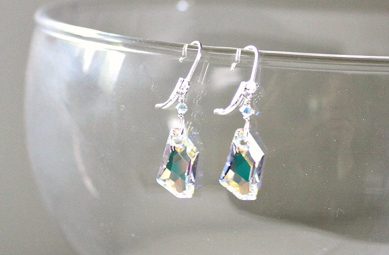 May include: A pair of silver dangle earrings with iridescent crystal drops. The crystals are faceted and have a green hue.