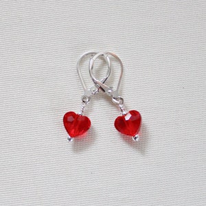 May include: A pair of silver heart-shaped earrings with red crystal accents.