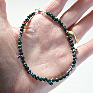 May include: A green and silver beaded bracelet with silver flower charms. The bracelet is made with small, round beads and has a silver clasp.