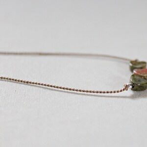 May include: A delicate necklace with a brown cord and five green and red gemstone heart-shaped beads.