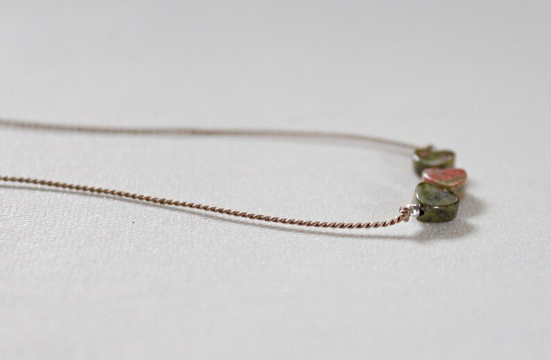 May include: A delicate necklace with a brown cord and five green and red gemstone heart-shaped beads.