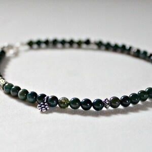 May include: A green and silver beaded bracelet with small silver charms. The bracelet is made with round green beads and has a silver clasp.