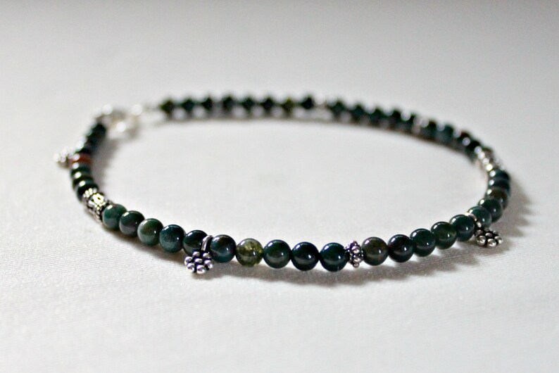 May include: A green and silver beaded bracelet with small silver charms. The bracelet is made with round green beads and has a silver clasp.