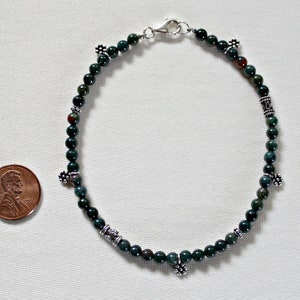 May include: A green and brown stone beaded bracelet with silver accents. The bracelet is about the size of a US penny.
