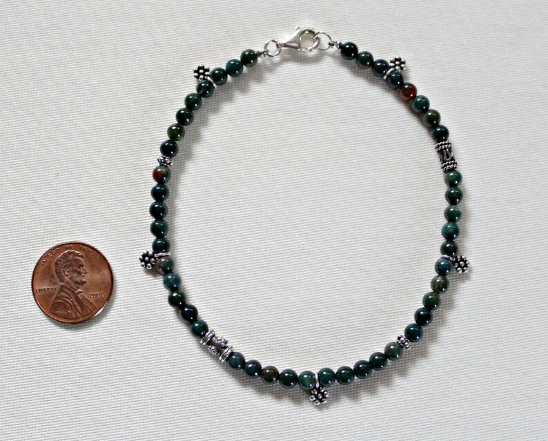 May include: A green and brown stone beaded bracelet with silver accents. The bracelet is about the size of a US penny.