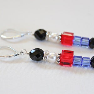 May include: A pair of dangle earrings with silver hooks and a red, white, and blue color scheme. The earrings feature black faceted beads, white pearl beads, and red and blue crystal beads.