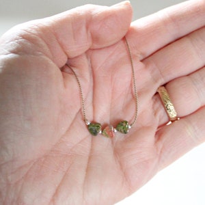 May include: A delicate gold chain necklace with three small, irregularly shaped green and pink stones.