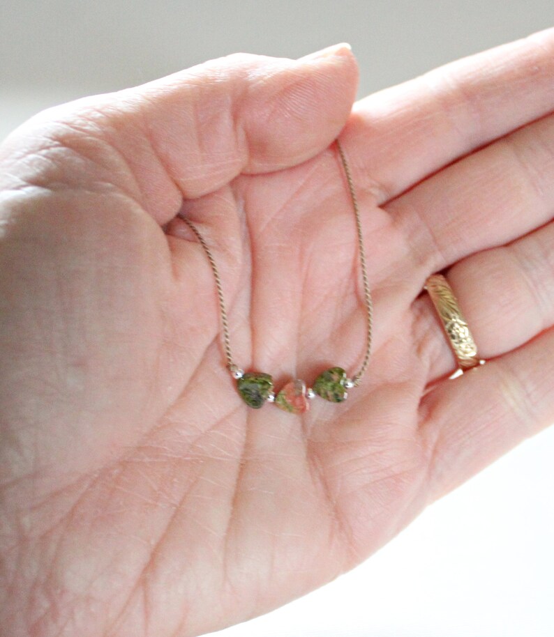 May include: A delicate gold chain necklace with three small, irregularly shaped green and pink stones.