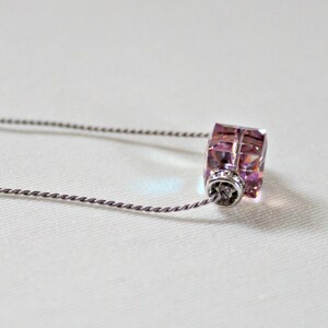 May include: A silver chain necklace with a pink crystal pendant. The pendant is a square shape with a faceted design.