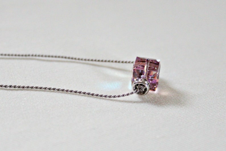 May include: A silver chain necklace with a pink crystal pendant. The pendant is a square shape with a faceted design.