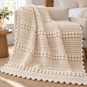 May include: A cream-colored crochet throw blanket featuring a textured pattern of horizontal bobble stitch rows alternating with sections of intricate, dense stitching and a scalloped edge border that frames the entire rectangular piece.