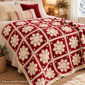May include: A handmade crochet blanket featuring a repeating pattern of cream-colored snowflake motifs centered within deep red square blocks, bordered by a cream-colored lattice. The blanket is draped over a bed with pillows.