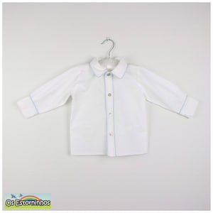 May include: White long-sleeved shirt with light blue trim on the collar, cuffs, and button placket. The shirt has a classic button-down design and is hanging on a metal hanger. The shirt is made of a soft, lightweight fabric.