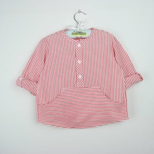 May include: A red and white striped shirt with a mandarin collar and a front pocket. The long-sleeved shirt has rolled-up cuffs and a button-down placket. The shirt is hanging on a metal hanger.