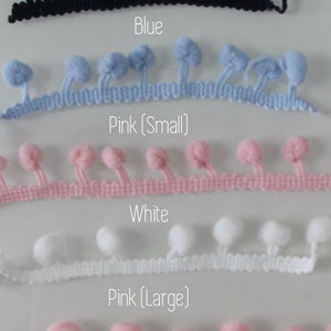 Op de afbeelding: Een selectie van pompom trim in marineblauw, blauw, roze (klein), wit en roze (groot). Elke trim heeft een rij kleine, pluizige pompons die aan een geweven basis zijn bevestigd. De tekst labelt de kleuren van elke trim.