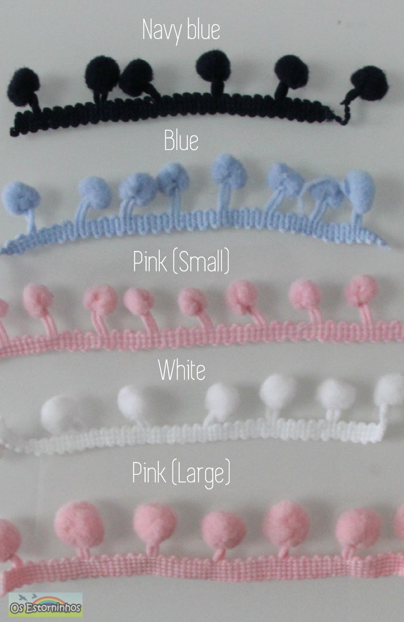 Op de afbeelding: Een selectie van pompom trim in marineblauw, blauw, roze (klein), wit en roze (groot). Elke trim heeft een rij kleine, pluizige pompons die aan een geweven basis zijn bevestigd. De tekst labelt de kleuren van elke trim.