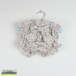 May include: A pair of baby bloomers with a floral pattern of red and blue flowers on a white background. The bloomers are ruffled at the waist and legs and are hanging on a hanger.