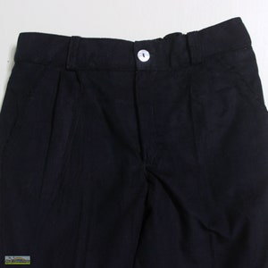 K&ouml;nnte beinhalten: Nahaufnahme einer schwarzen Cordhose. Die Hose hat einen Knopfverschluss und Falten auf der Vorderseite. Der Stoff hat eine gerippte Textur. Die Hose ist einfarbig schwarz.