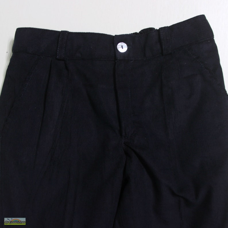 K&ouml;nnte beinhalten: Nahaufnahme einer schwarzen Cordhose. Die Hose hat einen Knopfverschluss und Falten auf der Vorderseite. Der Stoff hat eine gerippte Textur. Die Hose ist einfarbig schwarz.
