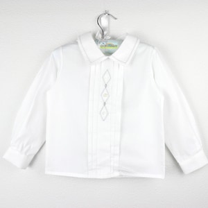 Può includere: Camicia bianca a maniche lunghe con colletto a punta e ricamo a diamante sul davanti. La camicia ha una chiusura con bottoni ed è appesa a un gancio di metallo. Il colletto e i polsini hanno un bordo cucito.