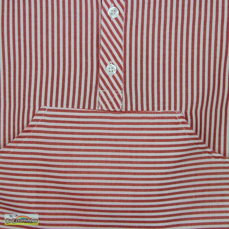 May include: Close-up of a red and white striped shirt. The shirt features a pocket and a button-down placket with two white buttons. The stripes are vertical on the main body and horizontal on the pocket.