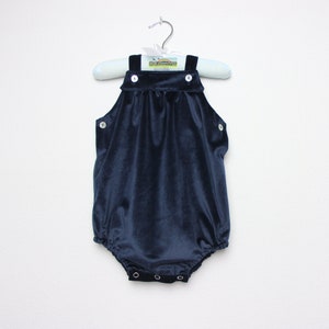 May include: A navy blue velvet romper with white buttons and a round bottom. The romper is hanging on a light blue and white striped hanger. The garment has a classic, timeless design.