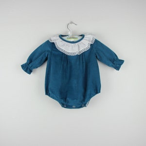 May include: Teal corduroy baby romper with long sleeves and a white lace collar. The romper has a button closure at the bottom and is hanging on a silver hanger. The sleeves have a ruffled cuff.