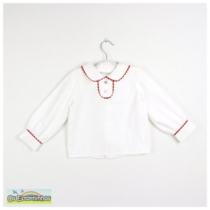 May include: White long-sleeved shirt with red trim on the collar, cuffs, and placket. The shirt has a Peter Pan collar and is hanging on a white hanger. The text "Os Estorninhos" is visible in the bottom left corner.