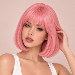 Op de afbeelding: Een schouderlange bob-pruik in een levendige pastelroze kleur, met een steile haartextuur en een volle pony die het voorhoofd omlijst. Het haar is glad gestyled en valt net boven de schouders met een lichte inwaartse krul aan de onderkant.
