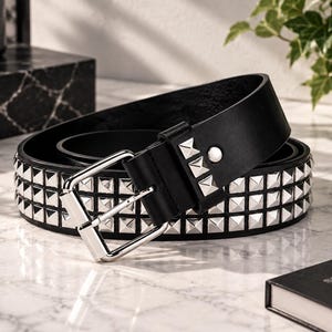 Peut inclure: Une ceinture noire ornée de trois rangées de clous pyramidaux carrés argentés. La ceinture comprend une boucle en métal argenté poli avec un cadre rectangulaire et un ardillon unique, conçue pour fixer la sangle via des trous pré-percés.