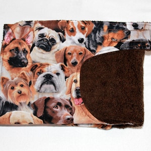 May include: A brown and tan fabric dish towel with a variety of dog breeds printed on it. The towel has a brown terry cloth backing.