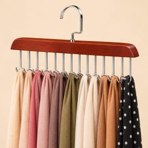 Könnte beinhalten: Ein Schalbügel aus Holz mit einem Haken aus poliertem Chrom und zwölf einzelnen Haken aus silberfarbenem Metall. Der Bügel präsentiert eine Auswahl an Schals in Beige, Rosa, Braun, Olivgrün sowie einen schwarzen Schal mit weißen Punkten.