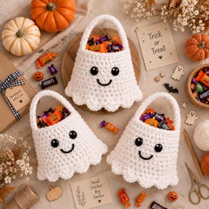May include: Three white crocheted ghost-shaped candy bags with black button eyes and stitched smiles. Each bag is filled with assorted Halloween candy. The scene includes pumpkins, a sign reading Trick or Treat, and a card saying Small Stitches Big Smiles.