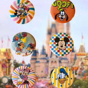 May include: Six circular pinback buttons featuring Disney characters. One shows a group of characters on a rainbow background, one features Goofy with his name, one shows Mickey and Minnie with balloons, one has Mickey on a checkered background, one shows Daisy and Minnie on a striped background, and one features Donald Duck on a yellow striped background.