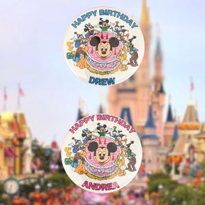 May include: Two circular pin-back buttons featuring a central illustration of Mickey Mouse on a pink birthday cake surrounded by Disney characters. The top button has blue text reading Happy Birthday Drew, and the bottom button has red text reading Happy Birthday Andrea.