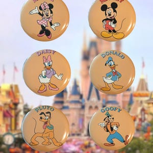 May include: A set of six round buttons featuring Disney characters on a tan background. Each button displays a character with their name printed above: Minnie, Mickey, Daisy, Donald, Pluto, and Goofy. The buttons have a glossy finish.