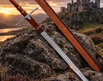 May include: A steel sword with a polished metal crossguard and a smooth, reddish-brown wooden handle topped with a silver-colored pommel. The sword rests alongside a matching reddish-brown leather scabbard on a dark, textured rock surface.